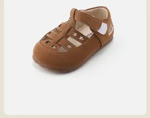 Detalle de sandalias de cuero marrón para niños con recortes de osito y cierre de velcro