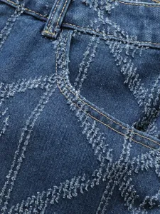 Macro detail of men's blue denim with unique frayed geometric patterns and stitching