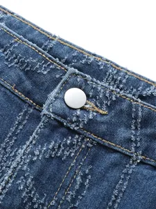 Close-up detail of blue distressed denim jeans featuring textured floral patterns and button.