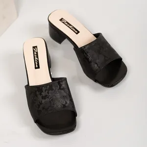 Close-up detail of black block heel slide sandals featuring an elegant floral embossed strap.