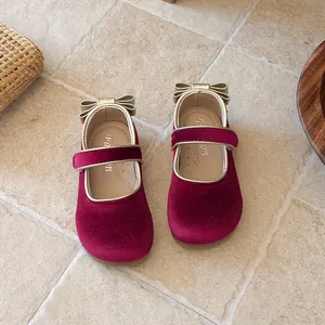 Detail view of girl's red velvet Mary Jane shoes with gold bow and velcro strap