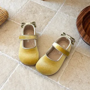 Close-up detail of yellow velvet girls' Mary Jane shoes with bow and velcro strap on tiles