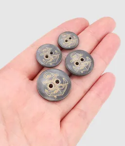 Macro detail of premium dark horn buttons with gold anchor engraving held in hand.