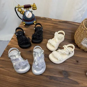 Top-down view of children's bow sandals in black, silver, and beige on a wooden table