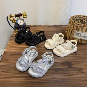 Detailed shot of girls' summer bow sandals in black, beige and silver colors on wooden surface