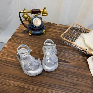 Close-up of silver girls' sandals with mesh butterfly bows on a rustic wooden tabletop.