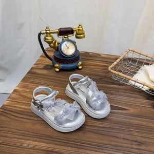 Detailed view of silver girls' sandals with mesh bows and white thick soles on a wooden table