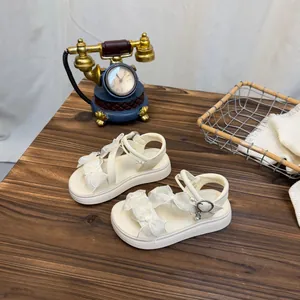 Detailed view of girl's off-white bow sandals on a rustic wooden table with vintage props.