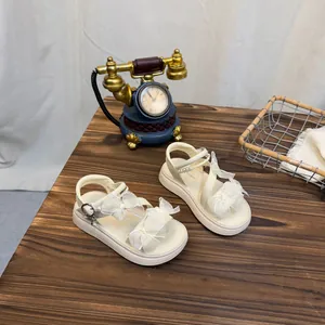 Detailed shot of cream girls' sandals with lace bow and pearls on a rustic wooden table