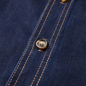 Close-up detail of a brown button and contrast stitching on a navy blue denim shirt