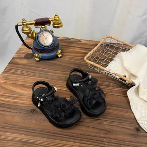 Black platform sandals for girls with mesh bows and pearl accents on wooden surface