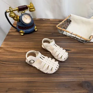 Beige gevlochten sandalen voor meisjes met gesloten neus op een houten tafel achtergrond