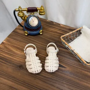 Gedetailleerd overzicht van gebroken witte gevlochten kindersandalen op houten tafel.