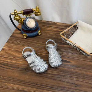 Bovenaanzicht van zilveren geweven koolsandalen voor meisjes op een houten tafelblad.