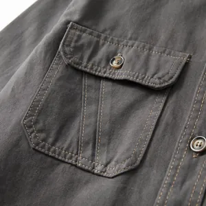 Close-up of grey cotton denim shirt pocket showing fine stitching and button detail