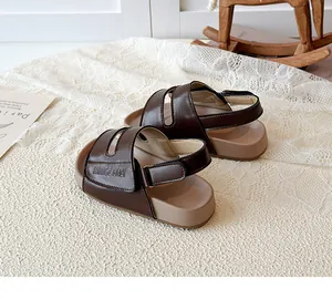 Nahaufnahme brauner Kinder-Sandalen mit Klettverschluss auf einem Spitze-Hintergrund