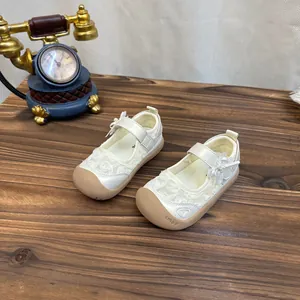 Detailed view of white floral lace girls' princess shoes with bow on wooden surface