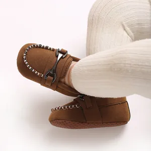 Close-up of brown faux suede baby moccasins with metal buckle and anti-slip sole