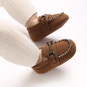 Close-up of brown suede baby loafers with metal buckle decoration and white stitching details