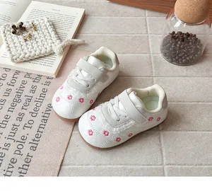 Dettaglio di scarpe bianche per bambini con ricami floreali rosa e pizzo decorativo.