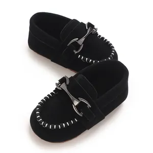 Close-up of black suede baby loafers with metallic horsebit buckle and white stitching