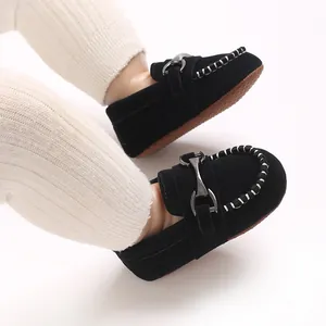 Detail shot of black baby loafers with metal horsebit buckle and white stitching.