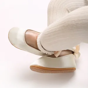 Detailaufnahme eleganter cremefarbener Prinzessinnen-Babyschuhe mit Perlen und Satinschleife.