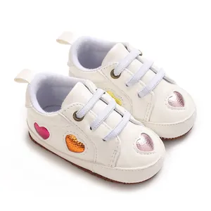 Vue détaillée de baskets blanches pour bébé avec des écussons en forme de cœur métallisés