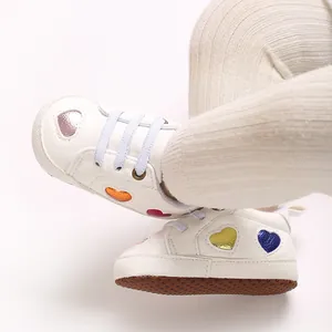 Détail de baskets blanches pour bébé avec des cœurs métalliques colorés découpés