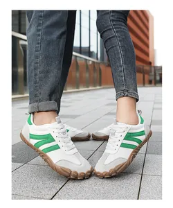 Detail of white barefoot sneakers with green stripes and wide toe box for walking.