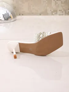 Detailed view of the sole and embroidered strap of white bohemian high-heel slippers.