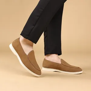 Bruine suède heren loafers gecombineerd met zwarte broek op een warme beige achtergrond