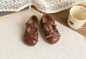 Detailed shot of brown British style girls faux leather Mary Janes with double bow design.