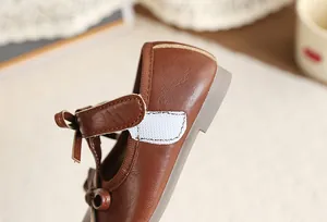 Close-up of brown girls' princess shoes featuring a delicate bow and Velcro strap.