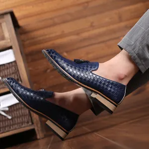 Detail view of men's blue woven tassel loafers worn with gray trousers on wood.