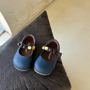 Detail van donkerblauwe Mary Jane kinderschoenen met sierkralen op getextureerd hout