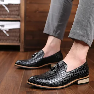 Side view of black men's woven leather loafers with decorative tassels on a wooden floor
