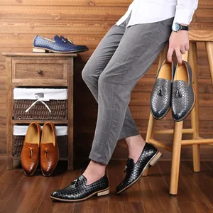 Elegant men's woven leather loafers with tassel detail shown in a wooden lifestyle scene.