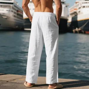 Back view of men's white loose-fit linen casual trousers at a sunny harbor scene.