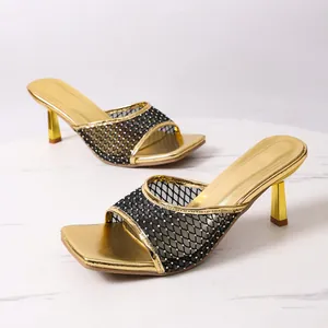 Dettaglio di eleganti sandali dorati con tacco alto, punta quadra e rete di strass.