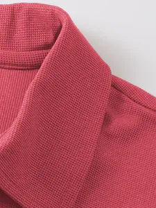 Gros plan sur la texture gaufrée premium d'un polo pour homme de couleur rouge.