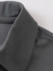 Gros plan sur la texture en maille gaufrée et le col côtelé d'un polo gris pour homme.