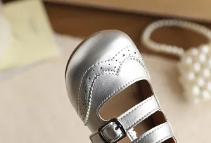 Close-up of silver girls Mary Jane shoes with elegant brogue detailing and buckles.