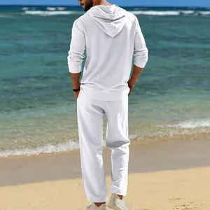 Rückansicht eines Mannes in weißem Leinen-Kapuzenhemd und Hose an einem sonnigen Strand