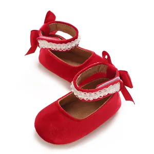 Detail of red velvet baby girl shoes with elegant bow and pearl strap.
