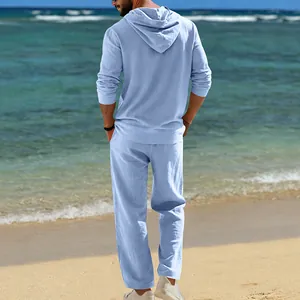 Rückansicht eines hellblauen Leinen-Kapuzenpullovers und einer Freizeithose für Herren am Strand