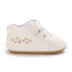 Detalle lateral de zapatillas blancas para bebé con bordado de flores rosadas finas