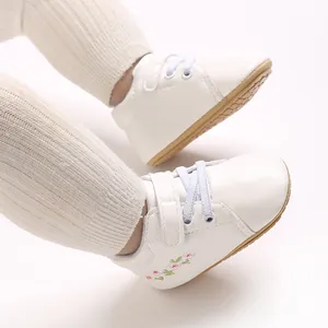 Vista detallada de zapatillas blancas para bebé con bordado floral y cierre de velcro