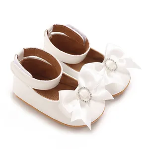 Detailansicht eleganter weißer Baby-Prinzessinnenschuhe mit Satinschleife und Strassring.