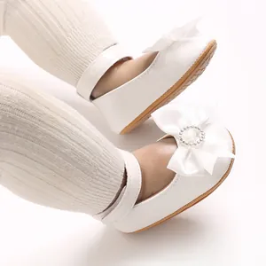 Detailansicht eleganter weißer Baby-Prinzessinenschuhe mit großer Satinschleife und Strass.